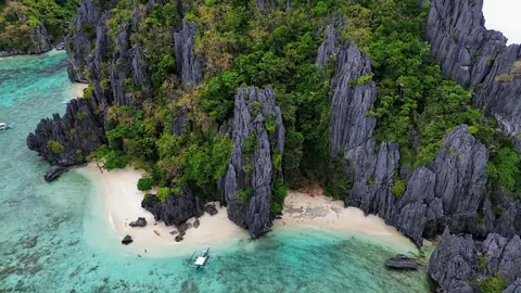 Aerial view of a secluded white-sand beach beneath tall limestone cliffs and coconut palms.